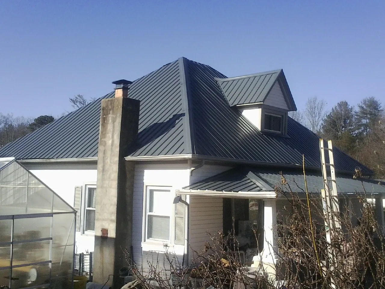 Dark blue standing seam metal roof on a white farmhouse with dormer — Slate & Tile Roof Repair by Roofing Brothers in South Butler