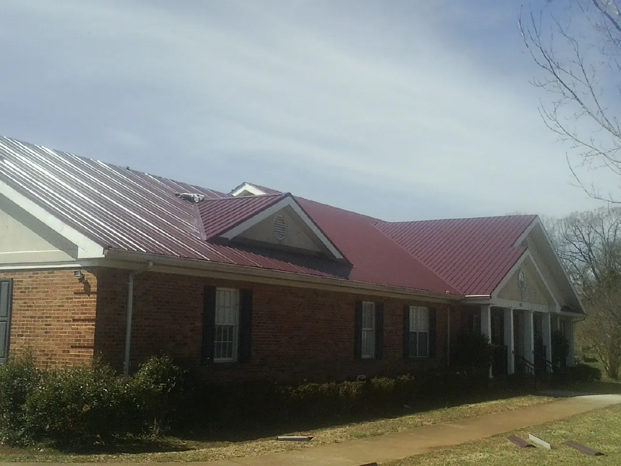 Red metal roof with gabled entries on a long brick building, from a Hail Damage Roof Repair job in South Butler