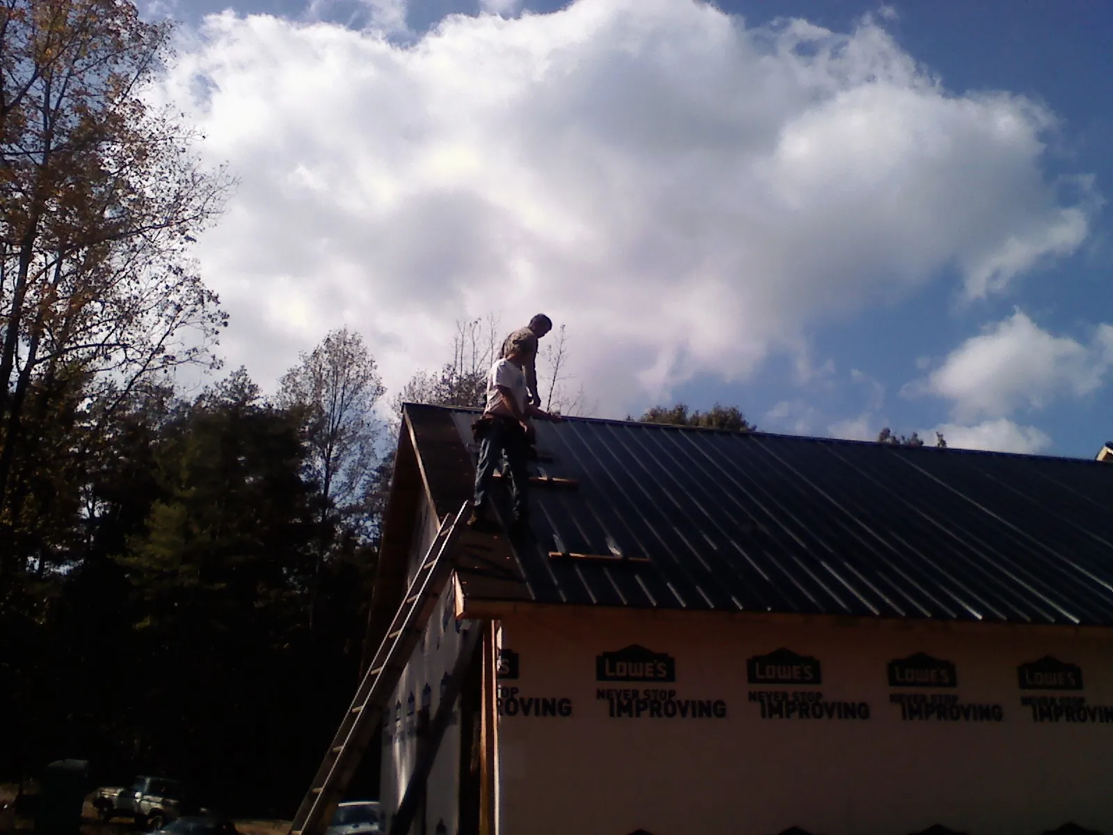Roofer fastening dark metal panels high against a cloudy sky, from a Roof Inspection job in South Butler
