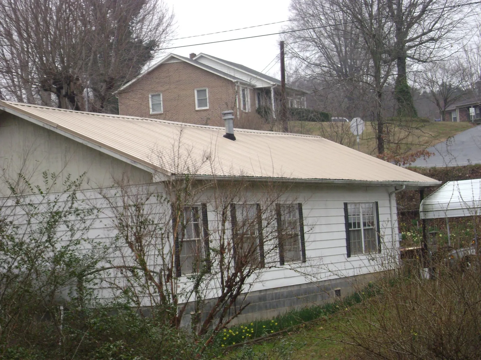 Tan metal roof on a white sided house set into a hillside — Commercial Roofing by Roofing Brothers in South Butler